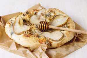 Whole Pizza with pear, gorgonzola and honey with olive wood honey dipper on baking paper over white wooden table.